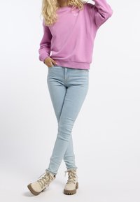 Růžová mikina s žebrovanými manžetami, světle modré úzké džíny a béžové turistické boty s tkaničkami a robustní podrážkou. Jednoduchý design, bez vzorů.