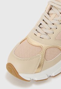 Sneaker beige chiaro con pannelli in rete, dettagli in pelle testurizzata e suola in gomma bianca. Presenta lacci piatti e un piccolo logo.