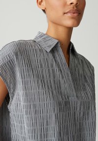 Blusa grigia a strisce con un sottile motivo testurizzato, maniche corte e colletto. Il tessuto ha una qualità leggera e traspirante.