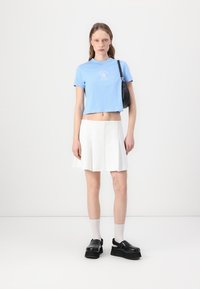 Light blue cropped t-shirt with graphic print, white pleated skirt, black chunky shoes, and ankle socks. Black shoulder bag details visible.