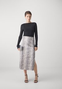 Black long-sleeve top with a boat neck, paired with a knee-length, textured, snake-print skirt featuring a side slit. Model holds a clutch.