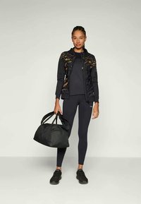 Jaqueta atlética preta com detalhes em dourado, top de manga longa preto, leggings pretas, tênis pretos e uma mala de esporte preta, tudo com um estilo elegante.