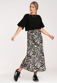 Czarny krótki top, długa spódnica z wzorem w czarno-biały wzór zebry, zestawione z czarnymi sneakersami z białymi paskami.