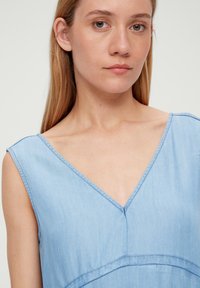 Jasnoniebieska, bezrękawnikowa sukienka z dekoltem w kształcie litery V i gładką fakturą. Posiada subtelne przeszycia i luźny krój.