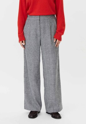 Persona vistiendo pantalones grises de cintura alta y pierna ancha, jersey rojo de manga larga y zapatos mocasines negros, de pie sobre fondo blanco.