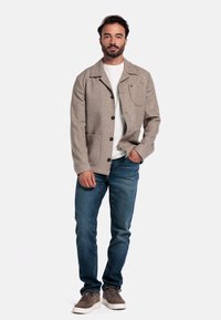 Grijs stoffen jasje met een kraag en voorzakken, in combinatie met een wit T-shirt en blauwe jeans, gedragen door een mannelijke model.