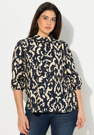 Blusa de manga abullonada en navy y crema con un audaz patrón abstracto, con cierre de botones en el frente y cuello redondo. Tela texturada con puños de mangas fruncidos.