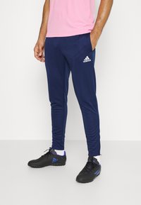 Pantaloni sportivi blu navy con tasche laterali e vestibilità affusolata; realizzati in un tessuto morbido. Indossati con scarpe sportive nere con dettagli blu.