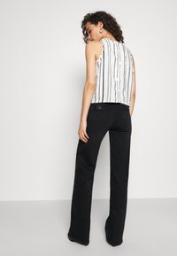 Lyhyt hihaton paita, jossa on pystysuorat mustat raidat valkoisella pohjalla, yhdistettynä korkeavyötäröisiin, levenevät mustiin housuihin.