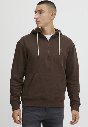 Brown zip-up hoodie with a front pocket, drawstring hood, and subtle logo detail. Made of soft, textured fabric. Pairing with gray jeans.
