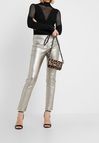 Černý síťovaný top s dlouhým rukávem a výstřihem do V, kombinovaný s metalickými stříbrnými upnutými kalhotami a malou kabelkou s leopardím vzorem. Černé sandály na vysokém podpatku.
