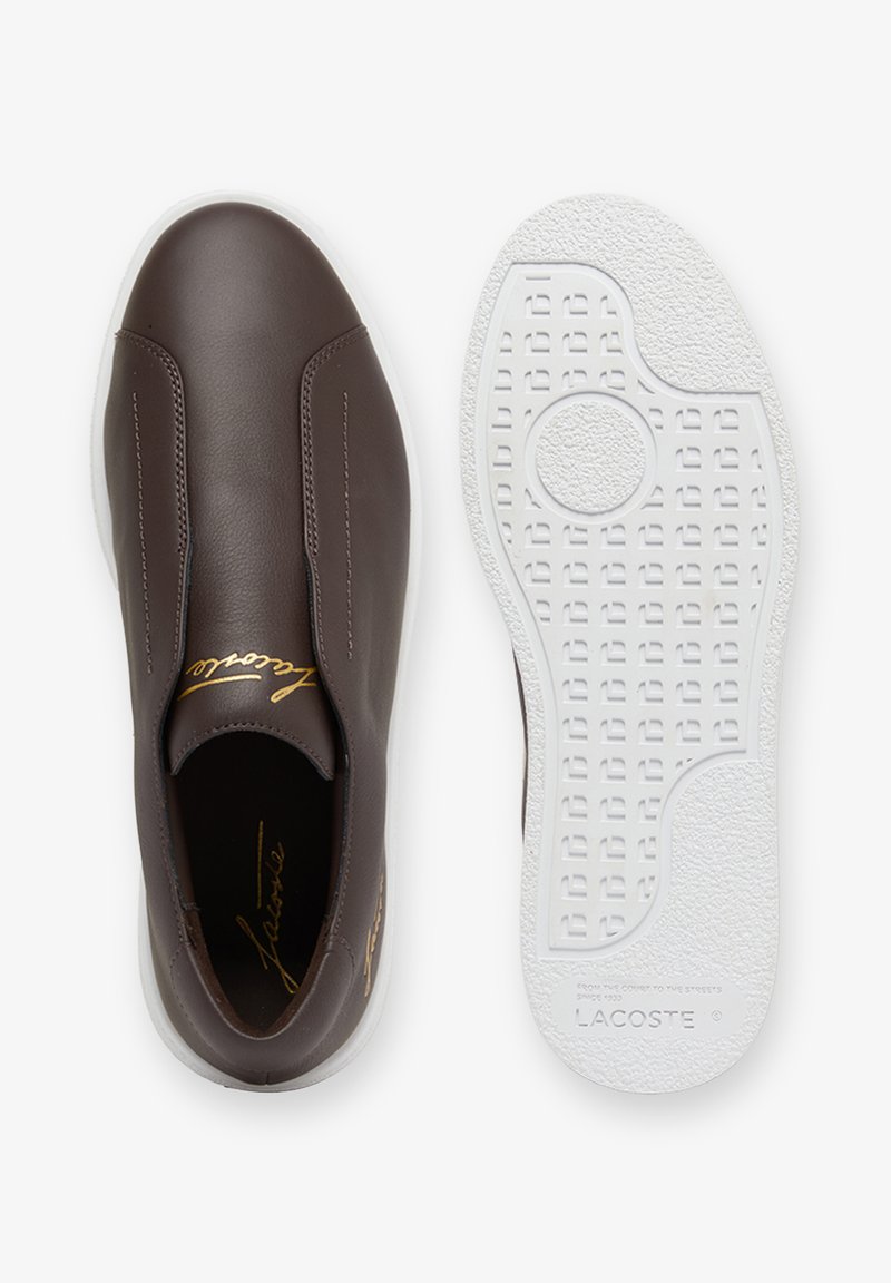 Sneaker slip-on marrone con tomaia in pelle liscia, firma Lacoste dorata all'interno e sulla linguetta, abbinata a una suola bianca testurizzata con motivo del battistrada.