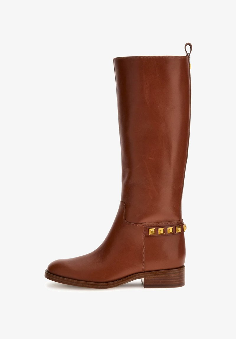 Botte en cuir marron haute jusqu'au genou avec un petit talon empilé et des clous carrés dorés près de la cheville du côté extérieur.