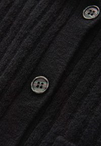 Dettaglio di un tessuto nero a maglia a coste con due bottoni rotondi a quattro fori con un motivo a strisce grigie e nere.