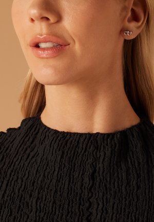 Boucles d'oreilles en argent en forme de cœurs entrelacés, présentées sur un tissu noir texturé. Fini lisse avec un éclat poli.
