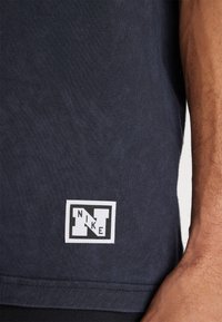 Mørk navy bomulds t-shirt med et hvidt rektangulært Nike-logo patch i kanten, med fin ribbet tekstur og afslappet pasform.
