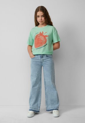 Mintgroene T-shirt met korte mouwen, voorzien van een grote rode aardbeienafbeelding met de tekst "STRAWBERRY-LICIOUS". Gecombineerd met high-waisted lichtblauwe jeans.