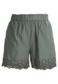 Shorts en coton vert avec une taille élastique, présentant un ourlet festonné orné de découpes circulaires et de clous décoratifs.