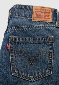 Τζιν παντελόνι με πίσω τσέπη που έχει χαρακτηριστικό V-ραφή, κόκκινη ετικέτα και ταμπά δερμάτινο λογότυπο με το όνομα και το λογότυπο της μάρκας.