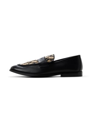 Mocasín de cuero negro con panel y detalle de correa de tela tejida en color beige, suela plana y punta redondeada, visto de lado sobre fondo blanco.