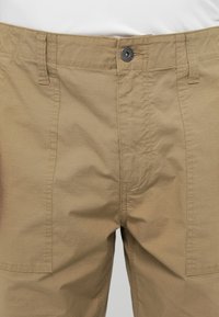 Beige cargo sort, gombos záródással, elülső zsebekkel, texturált anyagból, látható varrási részletekkel.