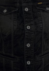 Black denim jacket featuring silver snap buttons, dual chest pockets, and a slightly textured fabric. G-Star logo visible at the collar.
