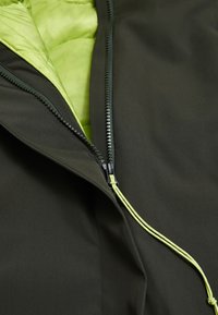 Dunkelgrüne Jacke mit teilweise geöffnetem Reißverschluss, der das hellgrüne gesteppte Innenfutter und eine passende hellgrüne Zugkordel zeigt.