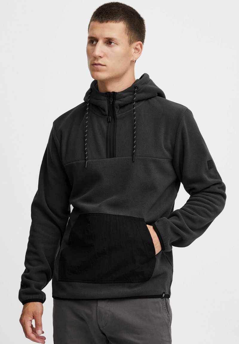 Donkergrijze fleece hoodie met een zwarte nylon voorzak, halve rits sluiting, verstelbare koordkap, en elastische manchetten.