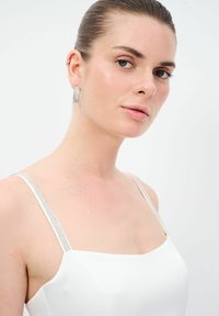 Bílé šaty s tenkými ramínky, zdobené třpytivými stříbrnými akcenty podél ramínek. Hladká tkanina a minimalistický design.