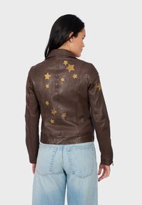 Veste en cuir brun ornée d'appliqués en forme d'étoiles dorées sur le dos et les épaules, avec une coupe ajustée et un col classique.