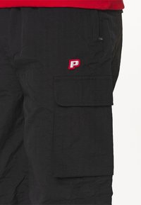 Shorts negri cargo din material ușor, având o buzunar lateral și un logo brodat "P" roșu, cu o textură finisată.
