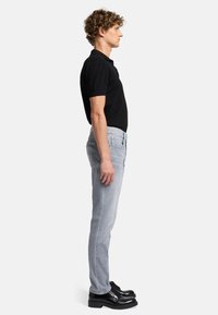 Polo shirt noir à manches courtes, jean slim gris clair, et chaussures à lacets noires vues de côté, présentant une tenue décontractée.