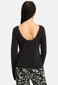 Schwarzes Langarmoberteil mit tiefem Rückenausschnitt, aus weichem Material gefertigt. Kombiniert mit floral gemusterten Hosen in Creme- und Schwarztönen.