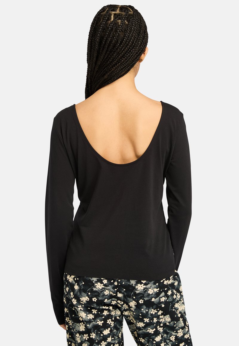 Top nero a maniche lunghe con scollatura profonda sul retro, realizzato in tessuto morbido. Abbinato a pantaloni con fantasia floreale nei toni crema e nero.