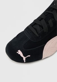 Črne z veliko blaga športne copate s pink poudarki na strani, teksturiranimi podrobnostmi in pink logotipom na prstu. Zavezovanje za varno prileganje.