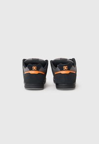 Zapatillas de skate negras con acentos naranjas, parte superior de ante y malla, cuello acolchado y suela de goma. Logo visible en la parte trasera.