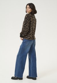 Pulover tricotat cu un model negru și maro, cu mâneci lungi, asortat cu jeans din denim cu picioare largi de culoare albastră și botine negre cu platformă groasă.