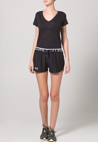 Czarny t-shirt z dekoltem w serek wykonany z lekkiego materiału, zestawiony z czarnymi sportowymi szortami z elastycznym pasem i logo, noszony z trampkami.