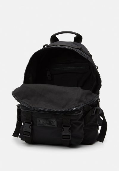 Rucksack negru din nylon, cu un compartiment principal cu fermoar, două buzunare frontale cu catarame și o mânere superioară. Textură netedă cu detaliu logo.
