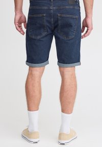 Tumši džinsa šorti ar savilktām aprocēm un divām aizmugurējām kabatām. Valkāti ar bēšām sporta kurpēm un baltām zeķēm.