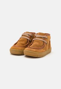 Bottes chevilles en suede marron avec un bout rond, semelle en caoutchouc beige et détails de lacets texturés. Elles présentent un col rembourré et des accents de couture sur les côtés.
