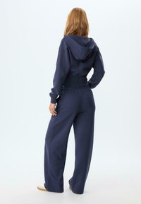 Felpa cropped blu navy con cappuccio, abbinata a pantaloni della tuta larghi. Il materiale sembra morbido con vita e polsini elastici.
