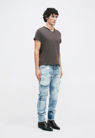 T-shirt cinza escuro de manga curta com decote em V, combinado com jeans claros desgastados e botins pretos de tornozelo; ajuste casual com bordas desfiadas e remendos.