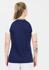 Musta urheilu paita, jossa on valkoiset lyhyet hihat, pyöreä pääntie ja slim fit -leikkaus. Ominaisuuksia ovat kuvioitu kangas, jossa on hienovarainen kiilto, ja erottuva kaulus.