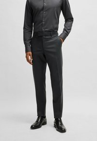 Pantaloni grigio scuro su misura con un design elegante, dotati di frontale piatto e tasche laterali, abbinati a scarpe in pelle nere.