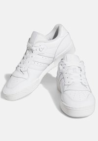 Vita atletiska skor i slätt läder med perforerade detaljer, som har platta snören, vadderad krage och gummisula.