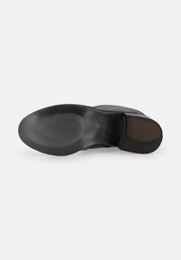 Suela de zapato de goma negra con una superficie texturizada y estriada, con un ligero tacón. Bordes planos y suaves con una impresión de logo central.