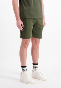 Olijfgroene katoenen shorts van textiel met een structuur, gecombineerd met een bijpassend t-shirt en witte sneakers. Zwarte en witte sokken met logo.