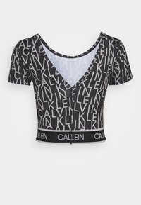 Sort cropped t-shirt med korte ærmer, der har en V-hals og gentagende hvidt logomønster. Elastikbånd nederst med branding.