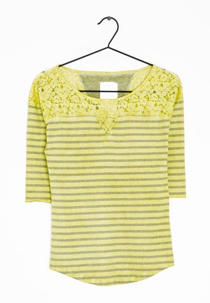 Haut pour femme rayé jaune et gris avec détail en dentelle sur le haut de la poitrine et manches trois-quarts, suspendu sur un cintre noir.
